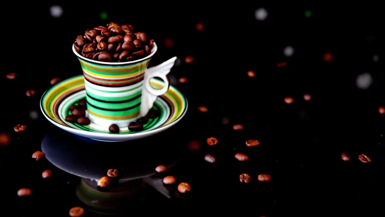 Roasted coffee beans beside a steaming cup